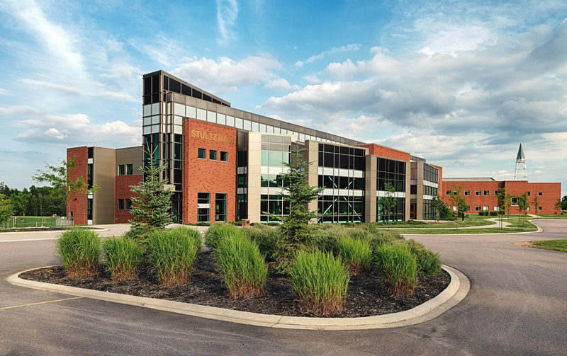 a modern, red brick academic building with many windows, set against clean grounds with green grass and blue sky
