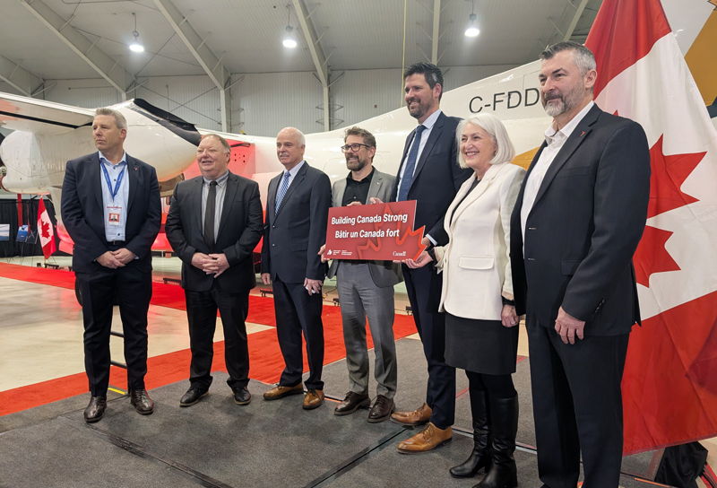 A group of people in a hangar, with an airplane in the background and a Canadian Flag