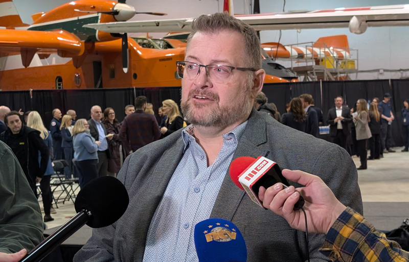 A man, Stephen Hale, taking questions from reporters in an aircraft hangar