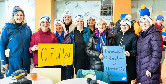 a group of women of various ages standing, wearing warm clothing and white toques, holding CFUW signs