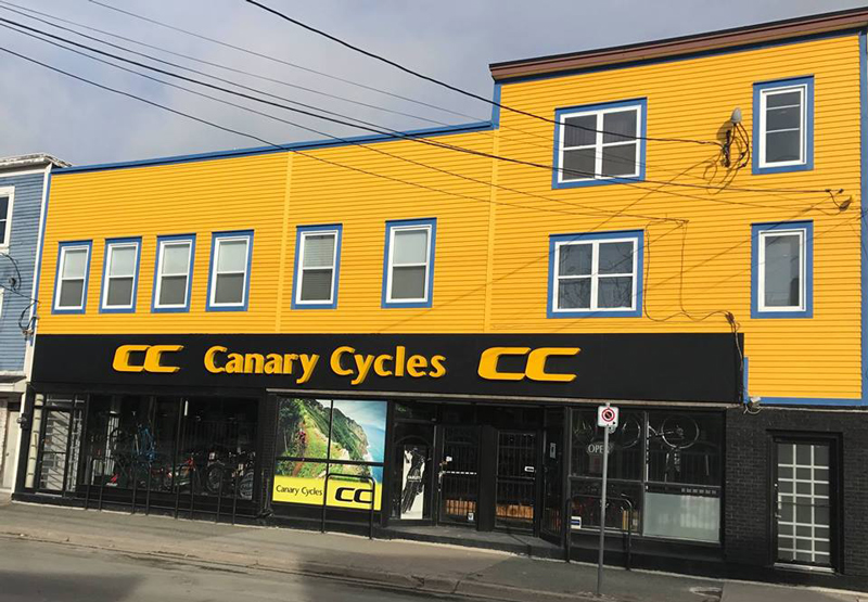 the front of Canary Cycles shop, a wide store front with bicycles in the windows and prominent branding outside with bright yellow paint