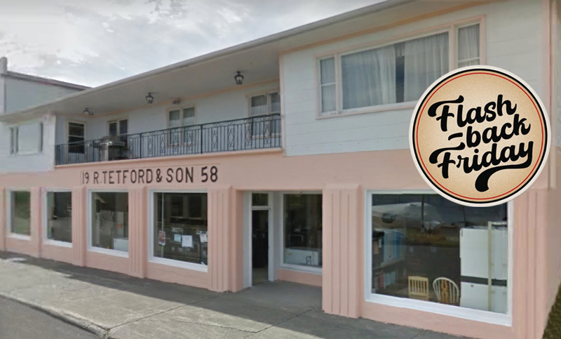 An exterior view of a 2 story building with a light peach colour first floor and white siding on the seconf floor, with a sign that says R. Tetford & Son, on a partly sunny day