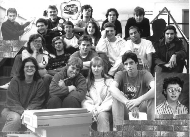 a large group of university age students seated and posing for a casual group photo, with 2 'pasted in' photos of students who were likely missing when the photo was taken. They are all smiling and clearly a close knit group