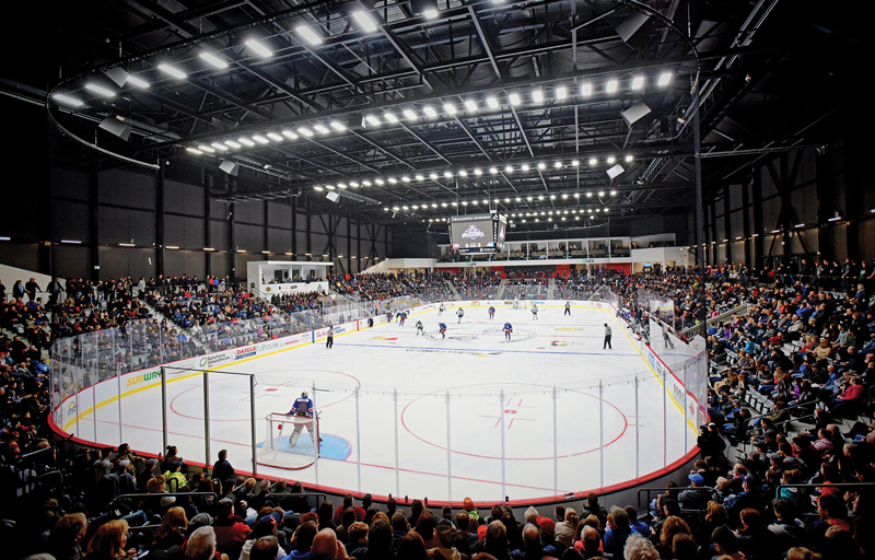 an interior shot, from behind the goal and up in the back, of a crowded hockey arena with a game taking place